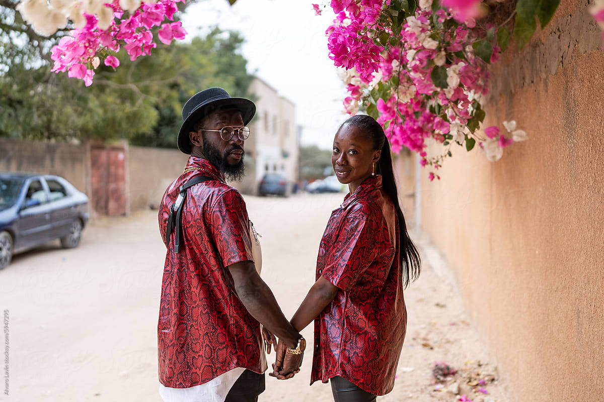Senegalese Couple Holding Hands Walking Along a Blooming Street in Day