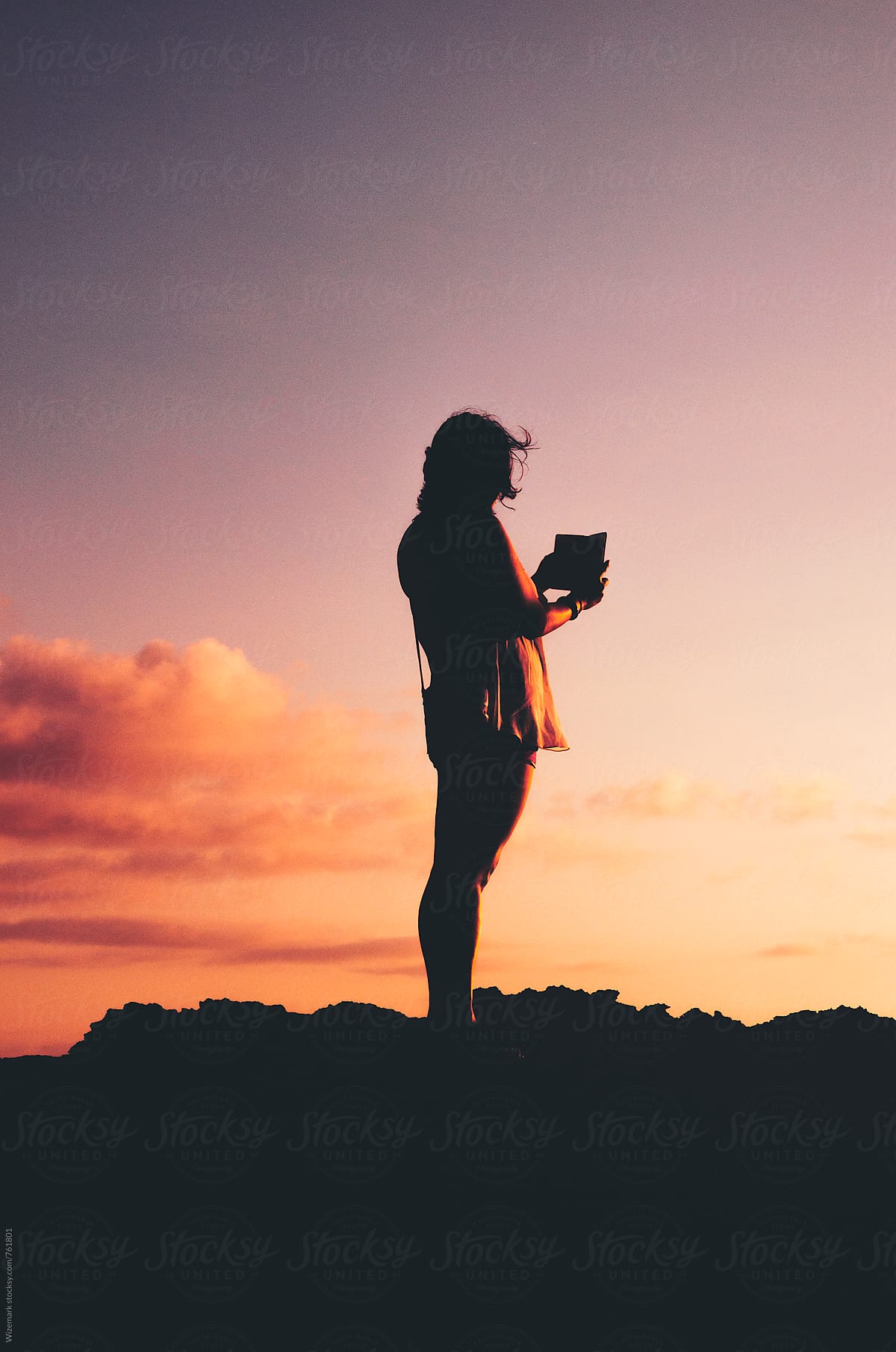 Anonymous, unrecognizable silhouetted female taking a photo of a beautiful sunset with smartphone