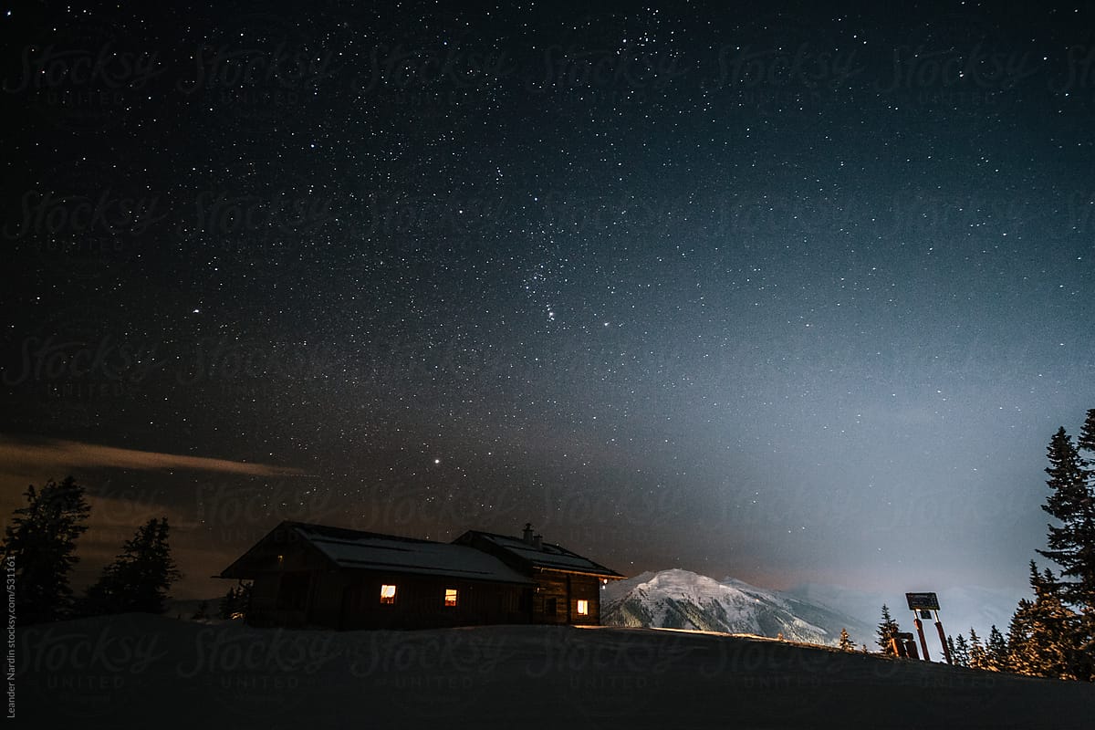 wooden alpine cabin in snowcovered mountain landscape at night under starry sky