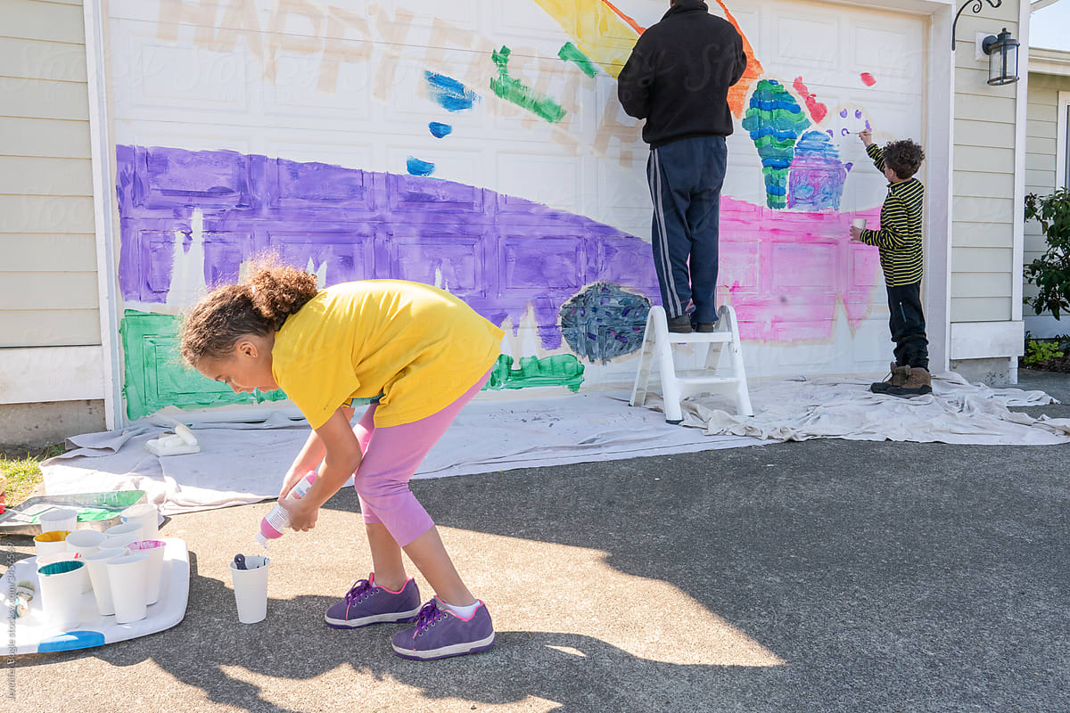 Girl fills paint cup while family paints mural