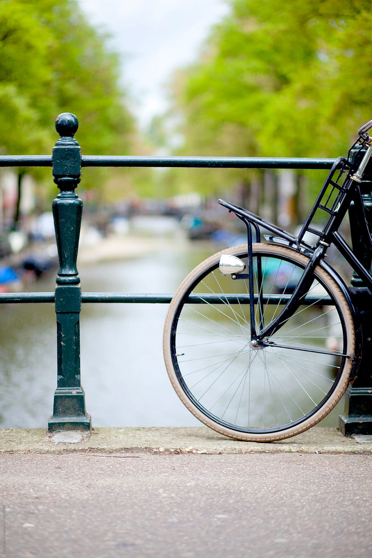 A classic bike standing on a bridge with an Amsterdam canal, trees and boats in the background
