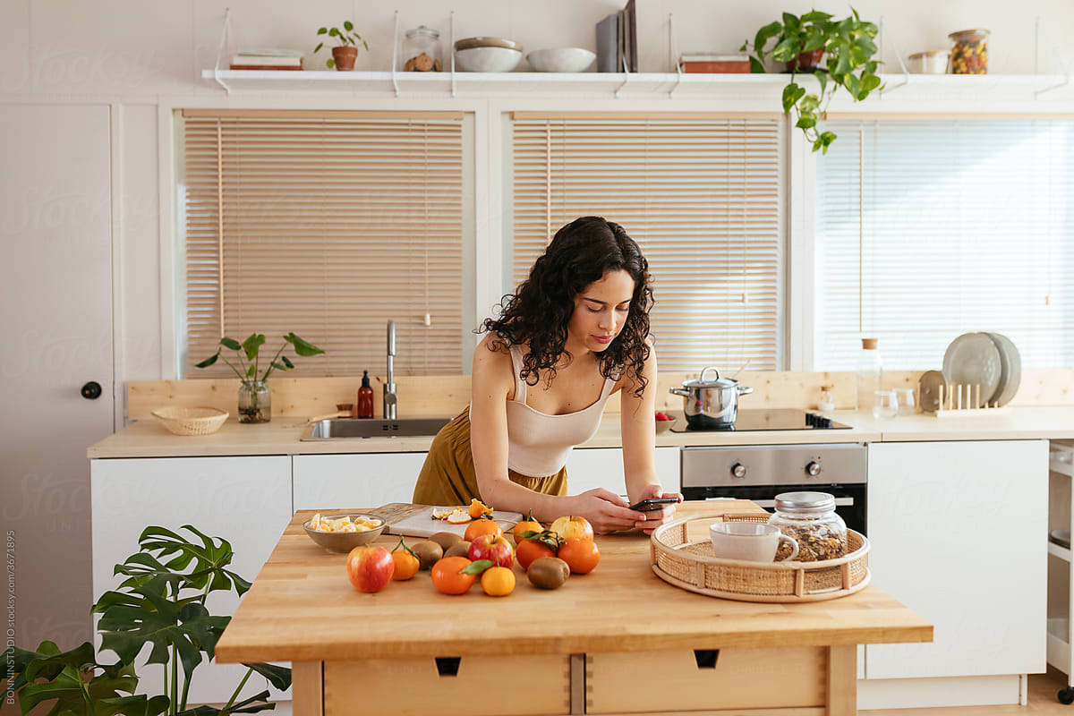 Young woman using smartphone near fruits in kitchen