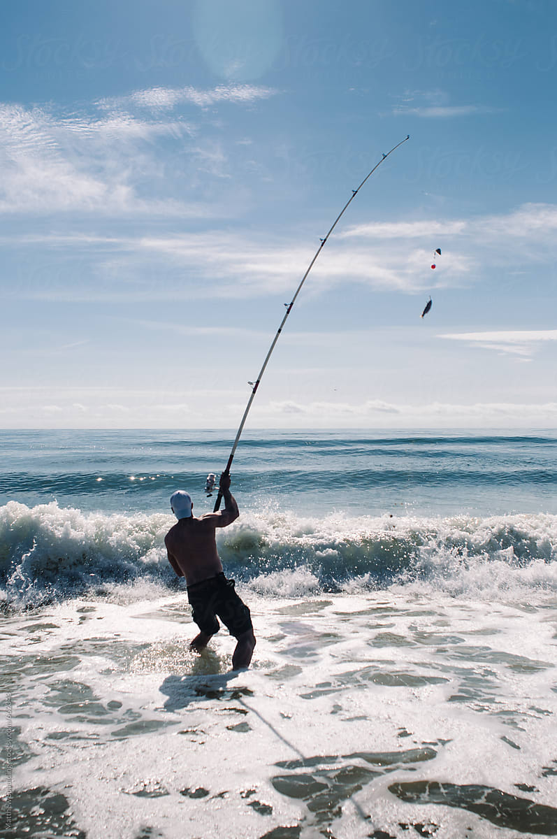 Man Casting Large Fishing Rod In Ocean Surf by Stocksy