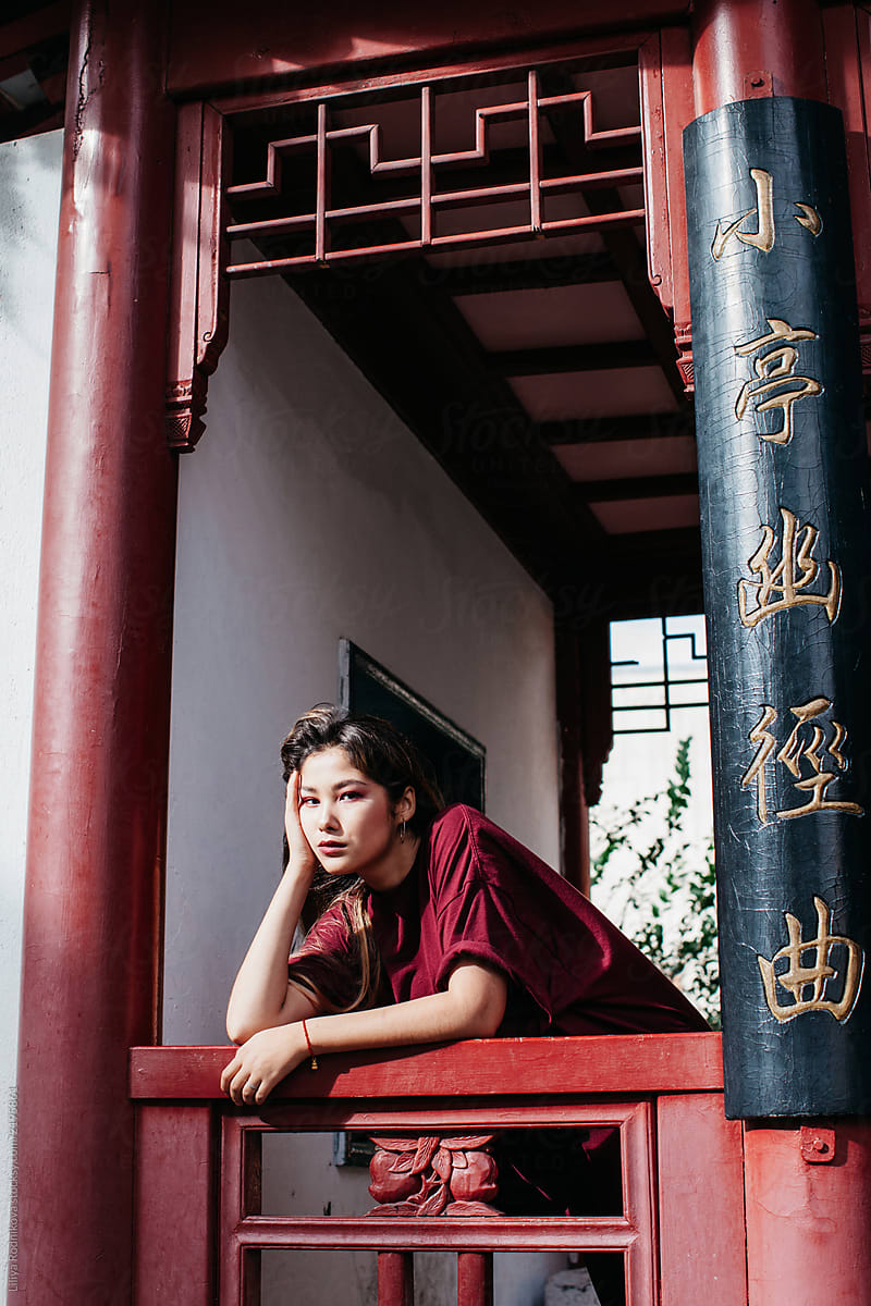 Fashionable young woman posing by asian style gazebo and looks bored