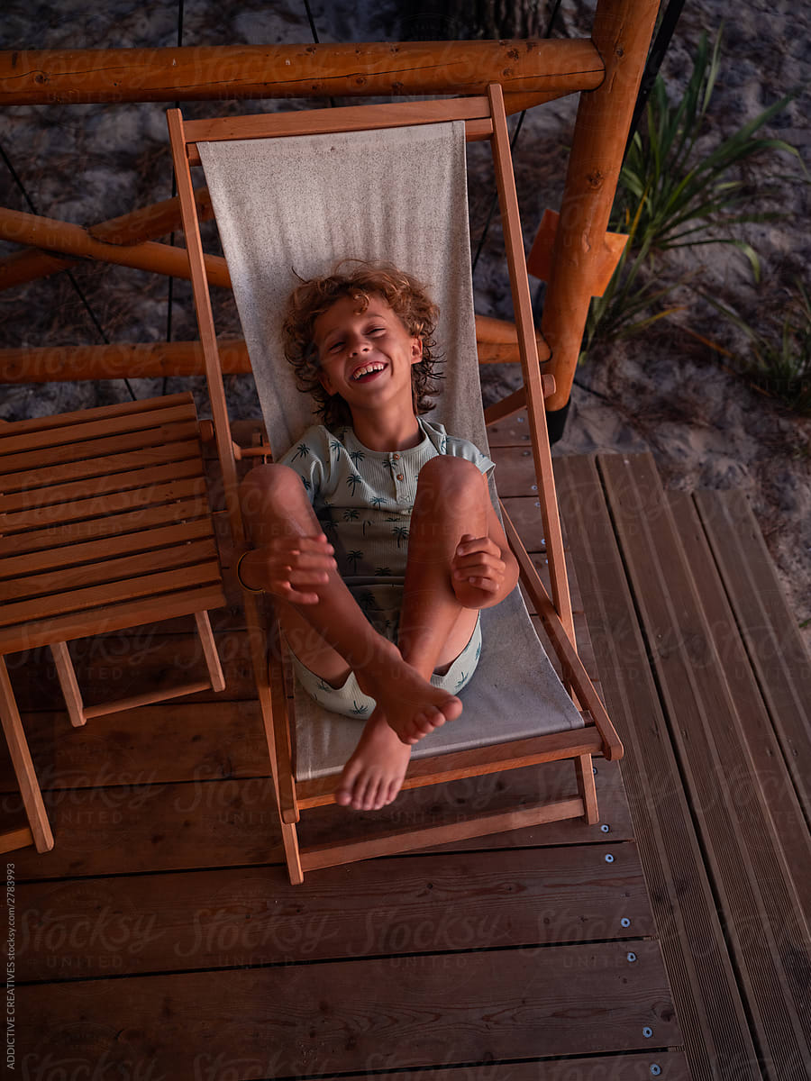 Barefoot Boy Enjoying On Deck Chair On Beach by ADDICTIVE CREATIVES