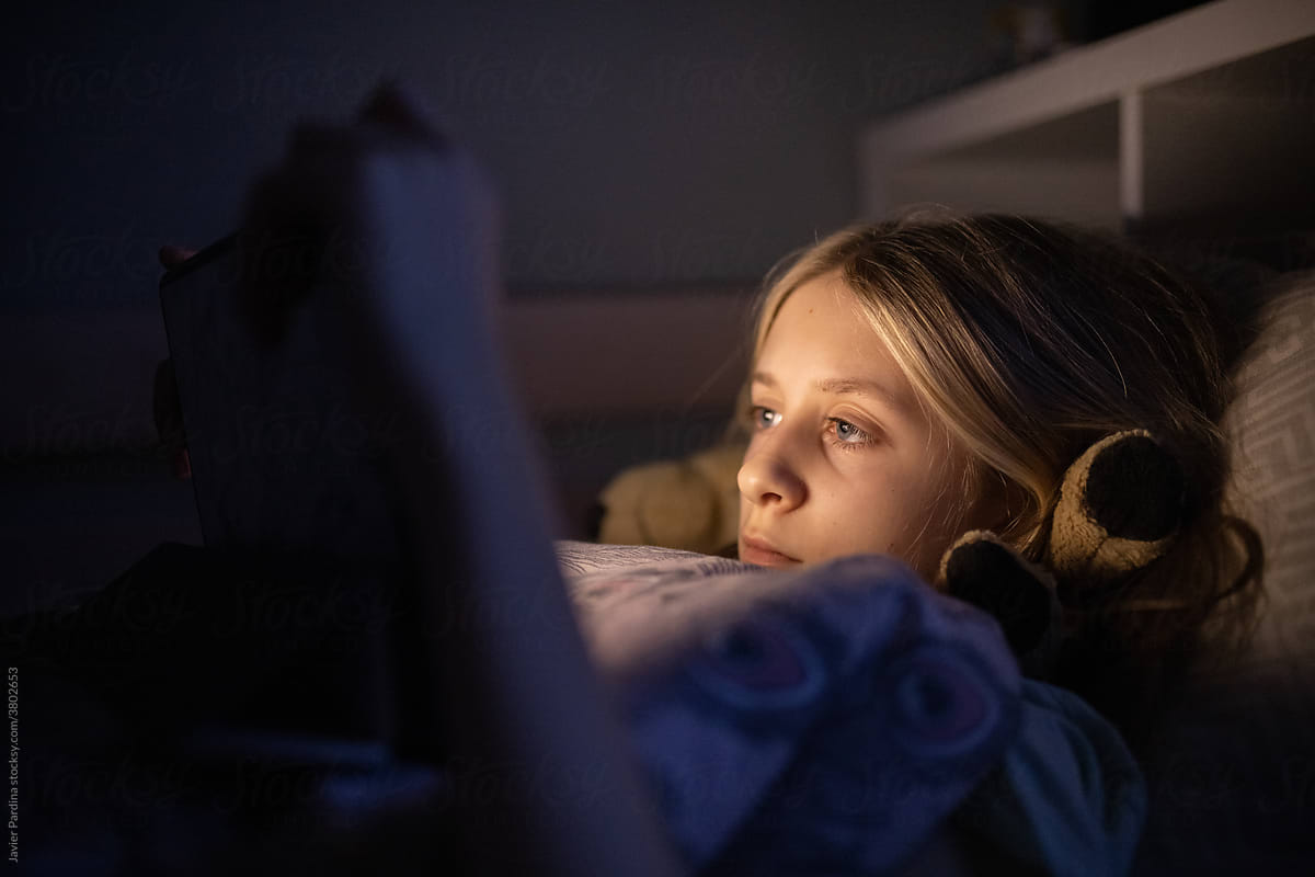 little girl lying in bed watching a movie