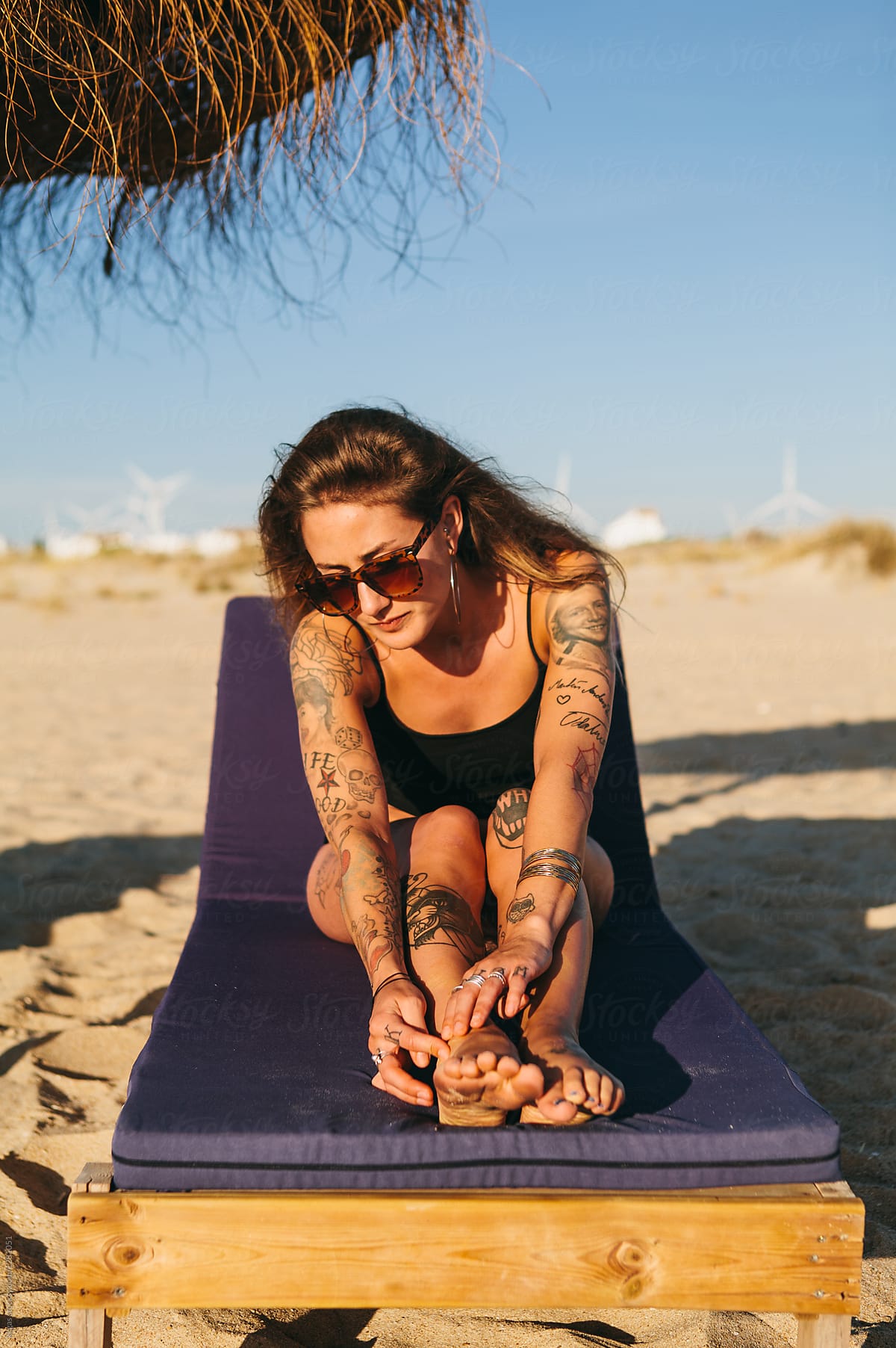 Beautiful tattooed woman sitting on a sunlounger on a beach