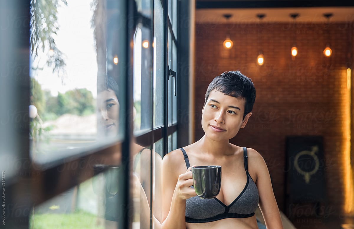 Short haired woman in a bra looking out the window