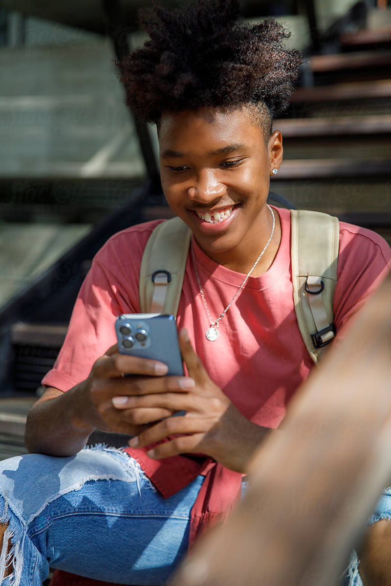 Happy afro student socializing on smartphone while sitting on steps