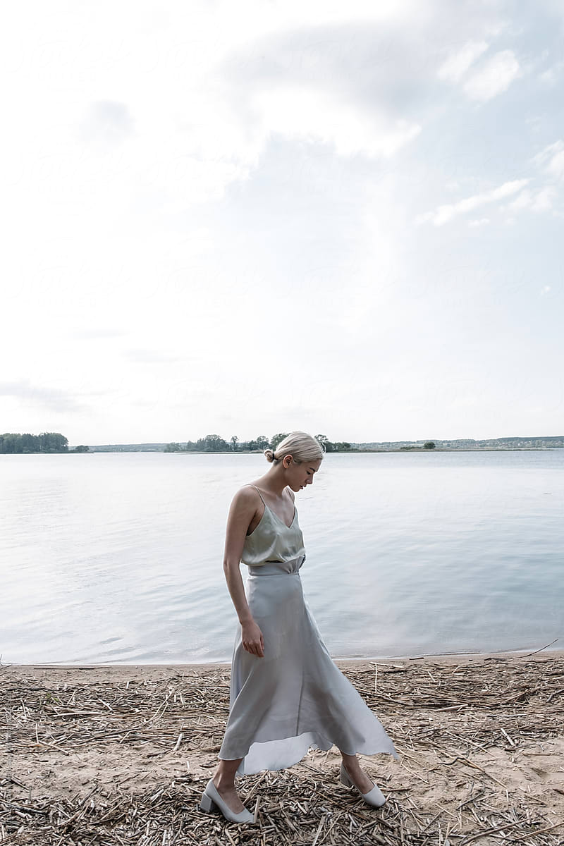 a girl with blond hair flying in the wind in a light dress on spaghetti straps against the backdrop of a lake in nature