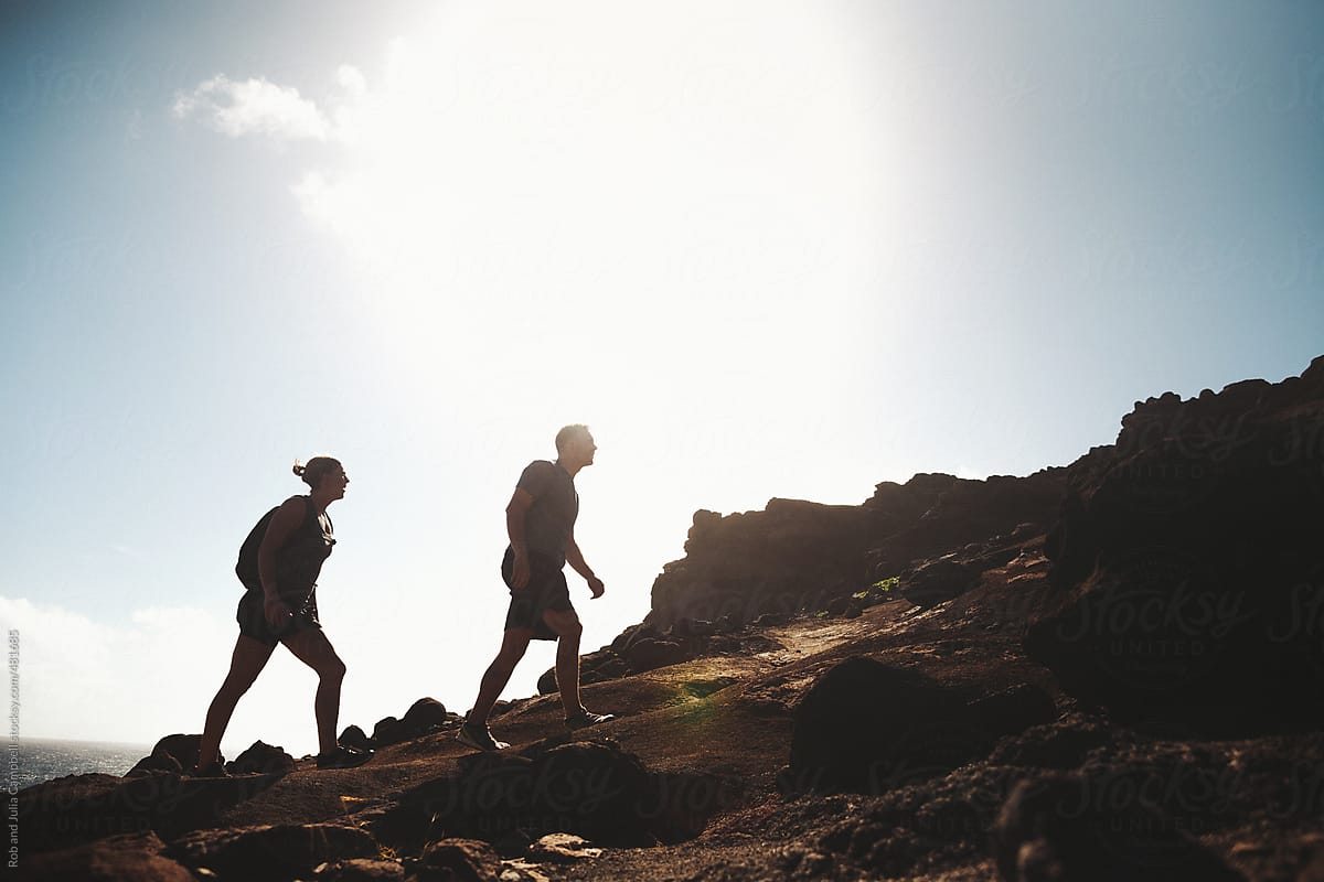 Silhoutte of young active couple hiking uphill in rocky landscape with sky and sun behind