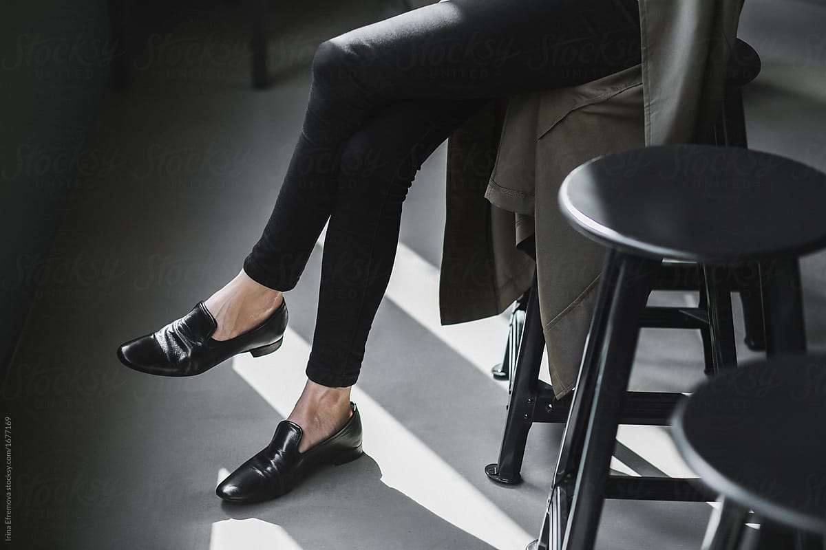 Black pants, black shoes on a black bar stool on a  gray floor
