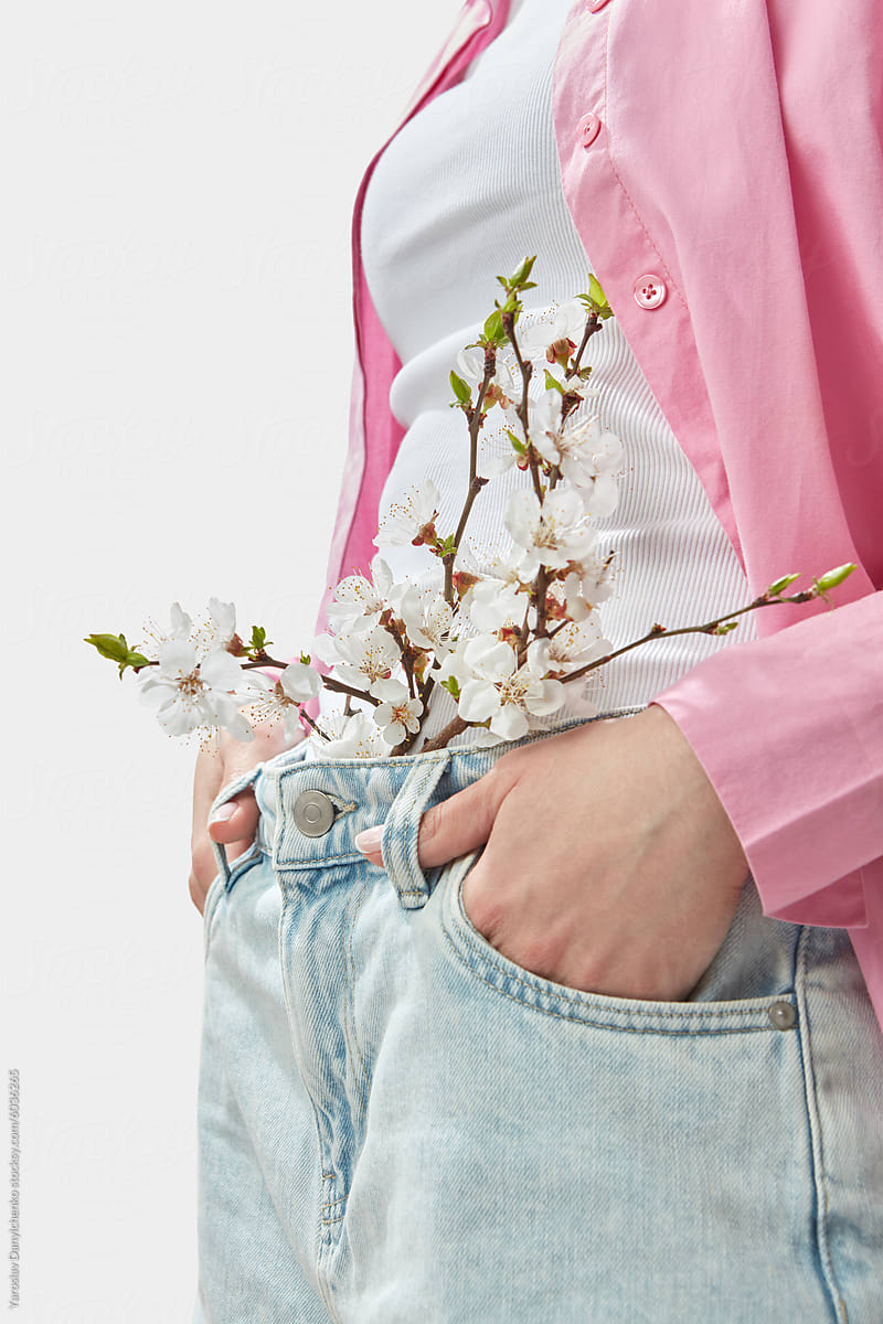Caucasian person posing with flowering branch tucked in waist of jeans