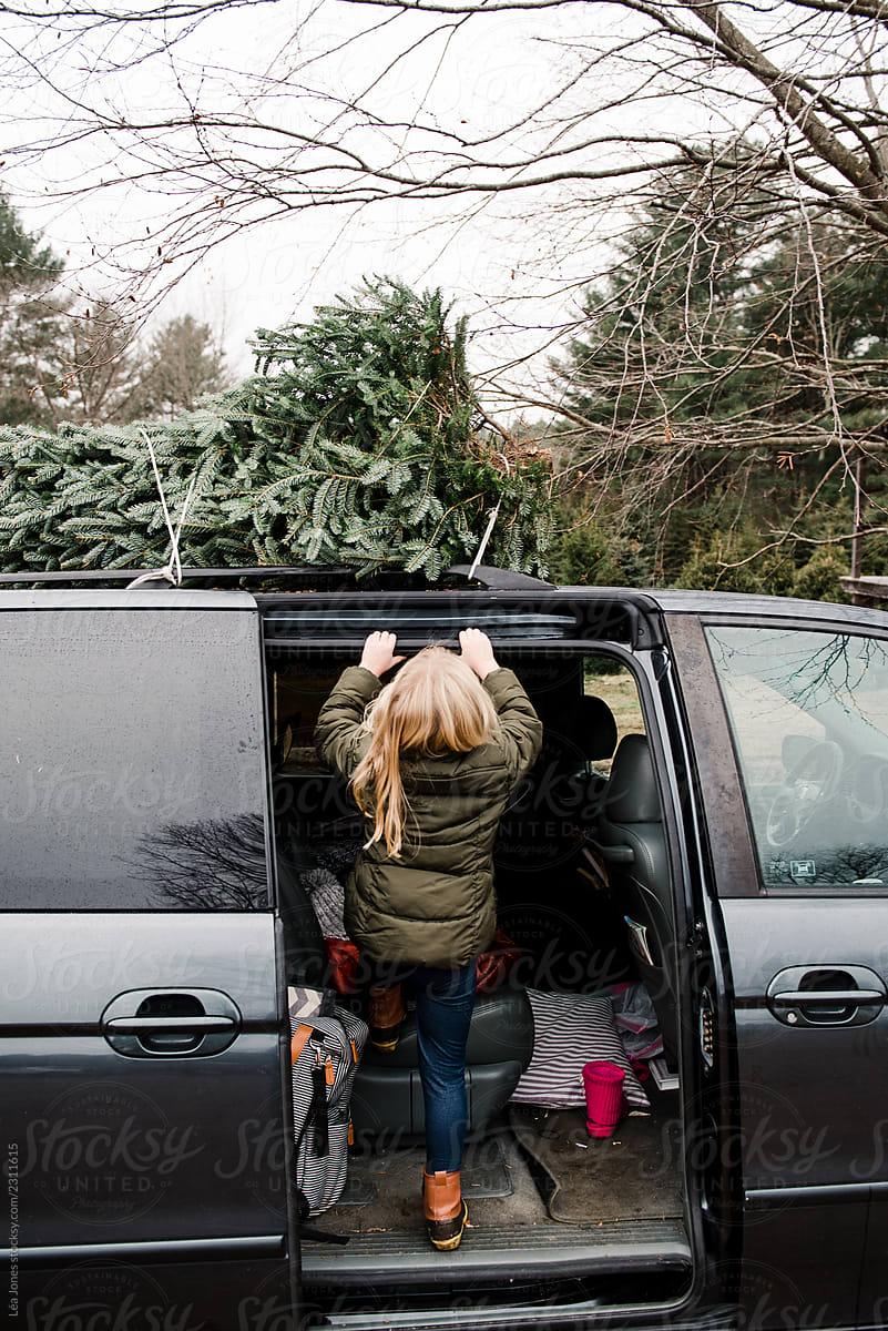 little girl climbing on car with Christmas tree on top