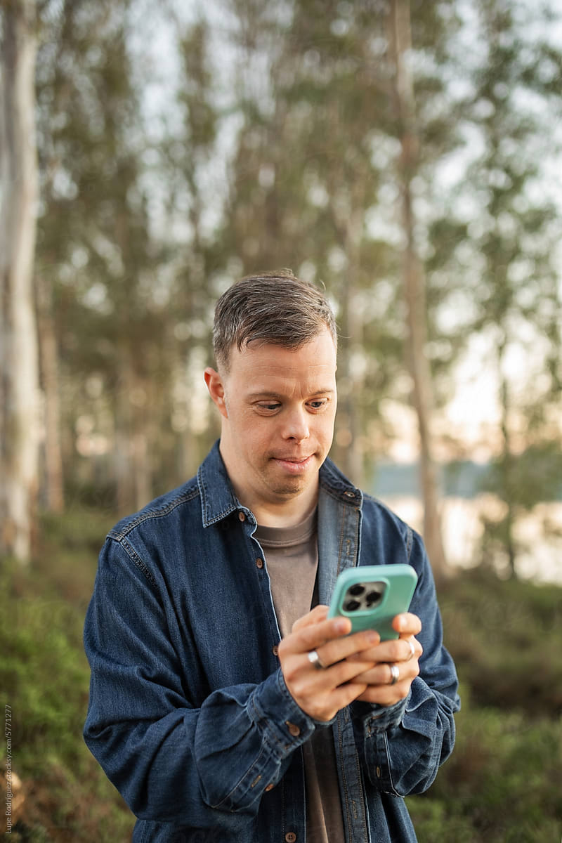 man with down syndrome using his mobile phone in a forest in nature