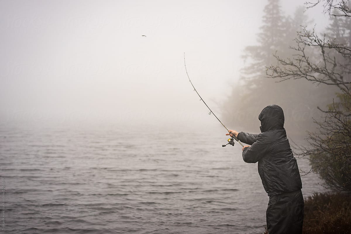 Man fishing in a mountain lake in bad weather.