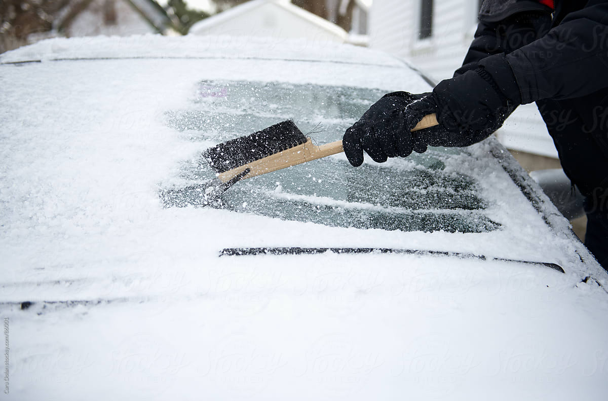 Man Using Scraper to remove Snow from Car Windshield