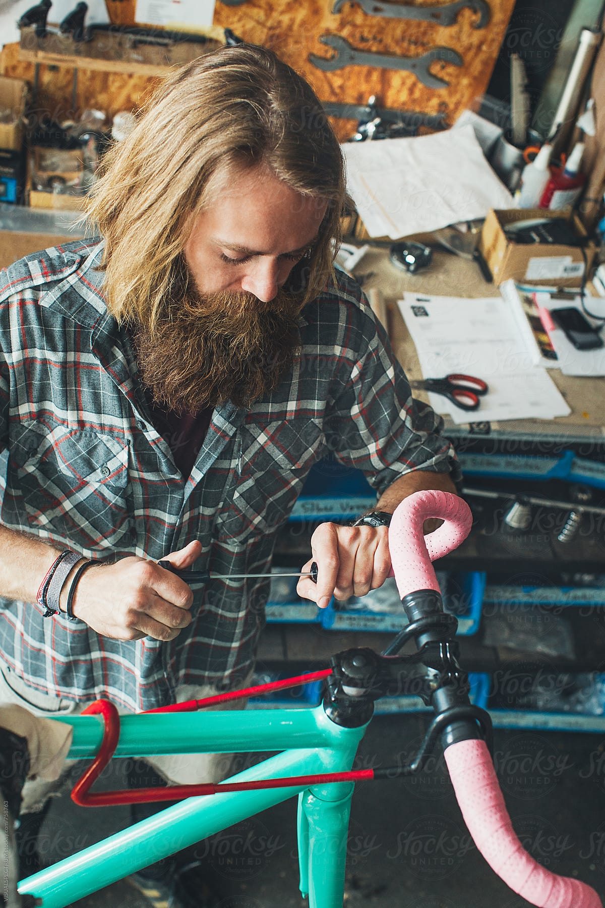 Long-Haired Hipster Bike Mechanic Using Screwdriver in Bright Workshop