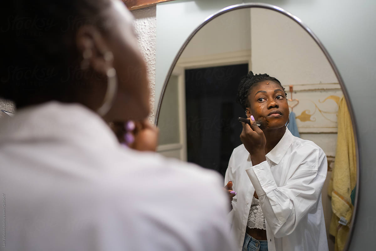 Black Woman Making Up In Front Of The Mirror At Home.