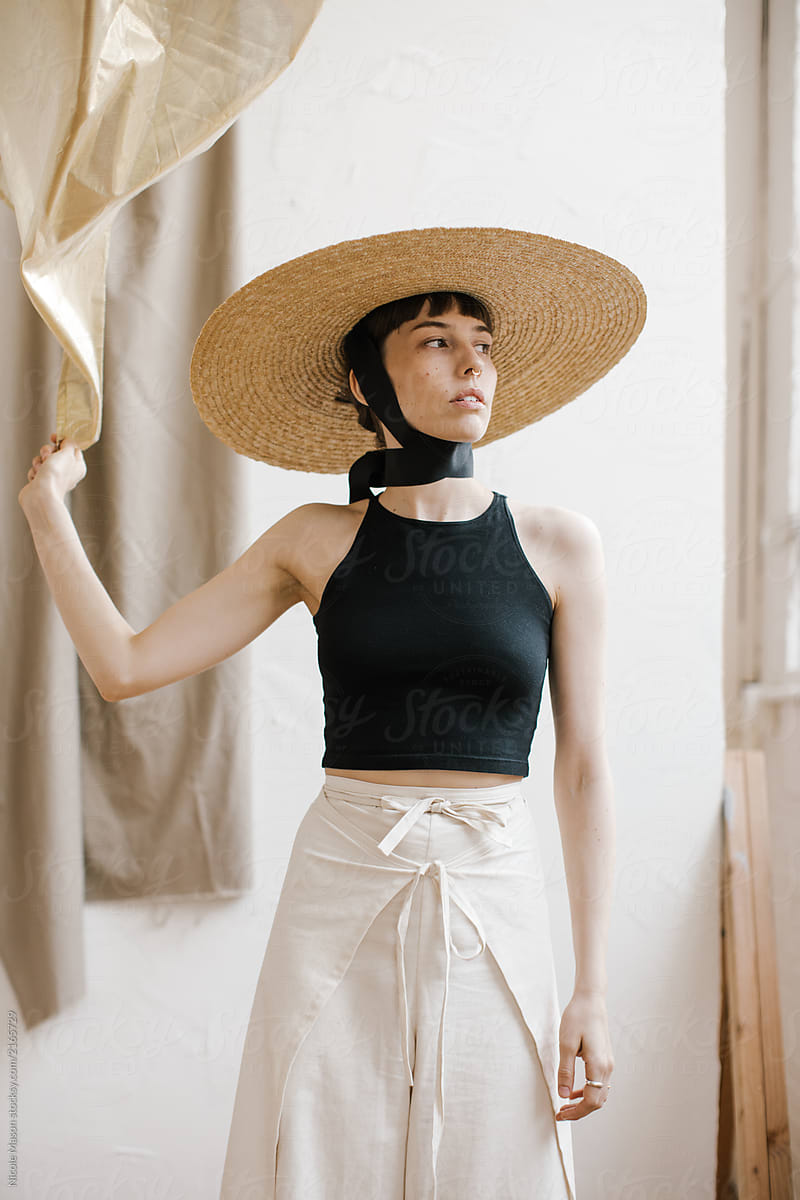 fashion model wearing large hat in studio holding sheer gold fabric