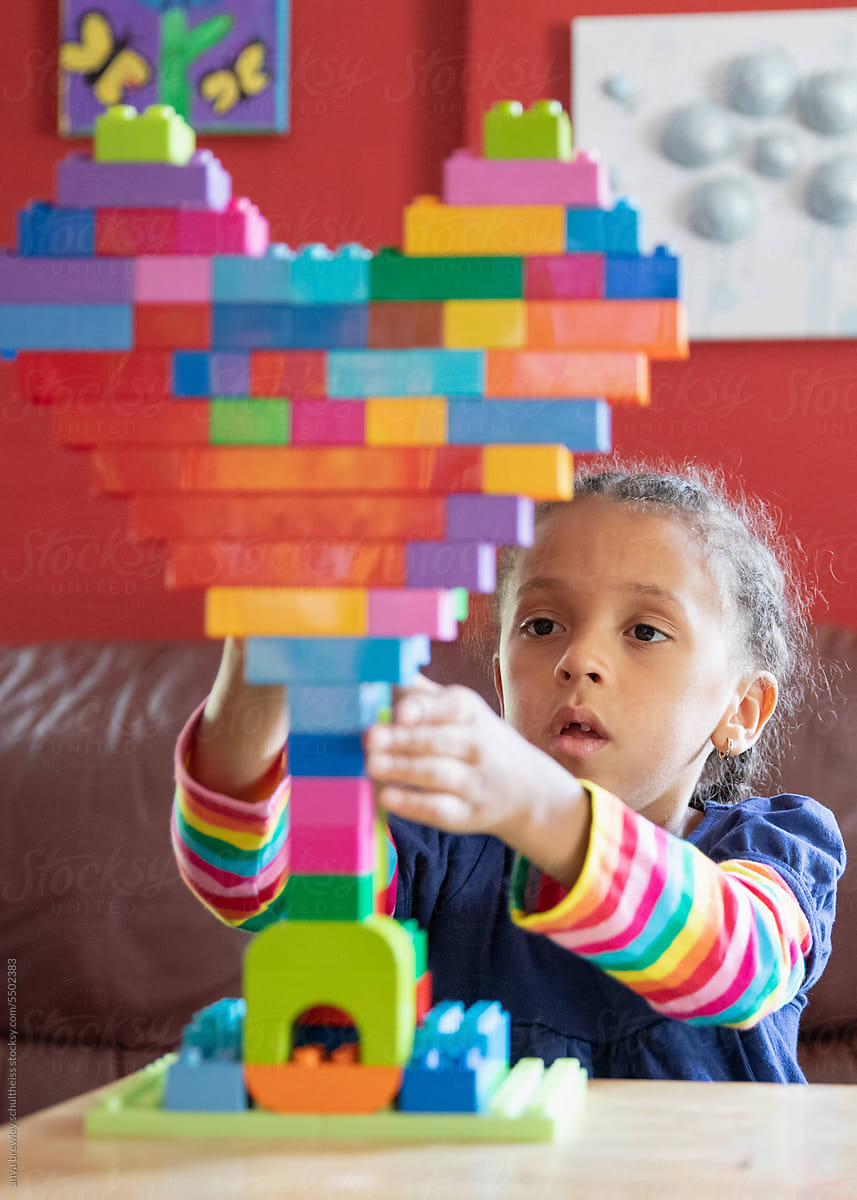Child building a heart with bright coloured lego blocks.
