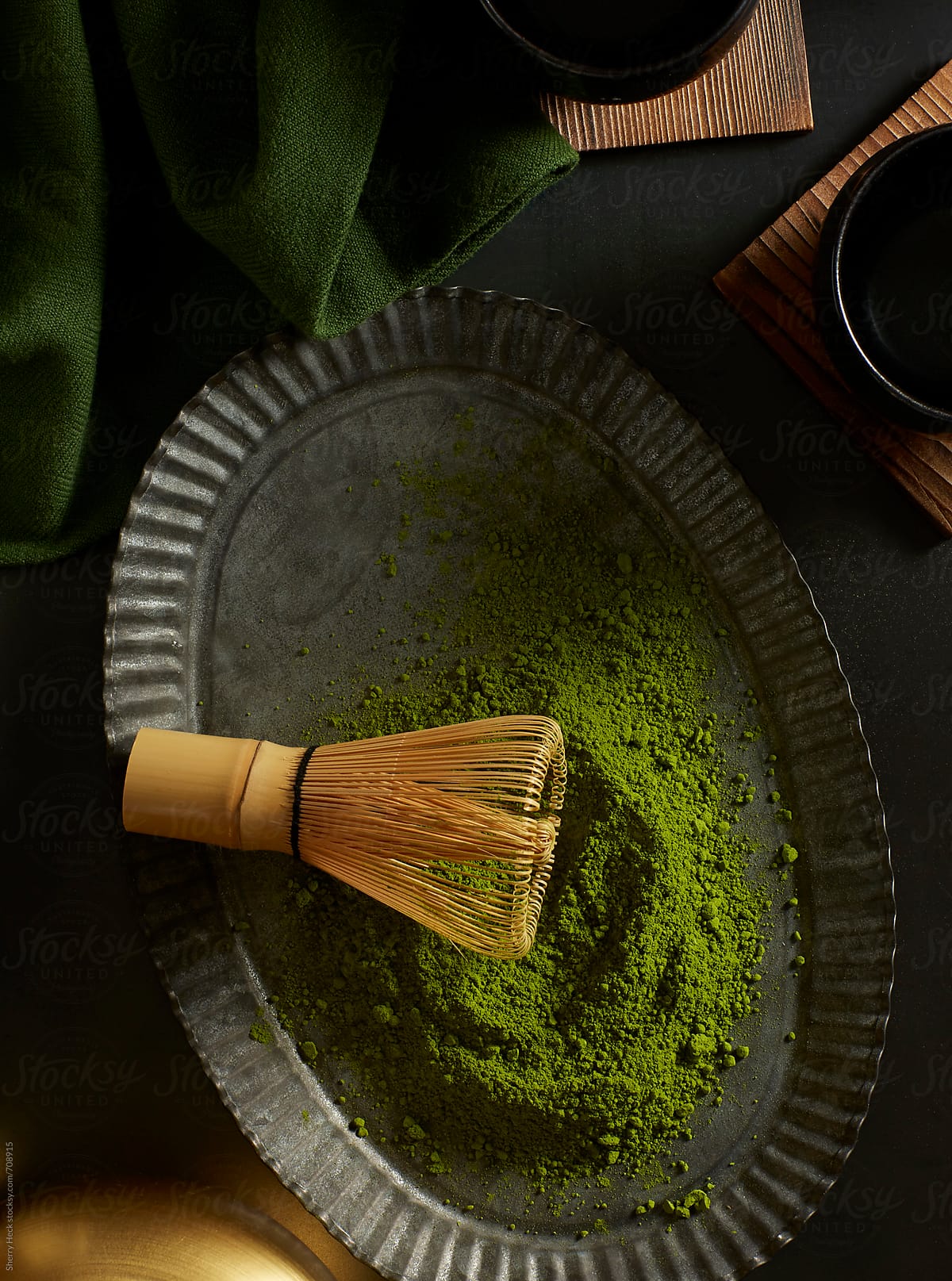 Green matcha powder with bamboo whisk on pewter plate