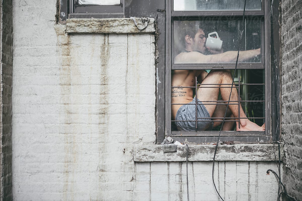 Shirtless Man in Boxer Shorts Drinking Coffee Sitting at Window of Urban Apartment