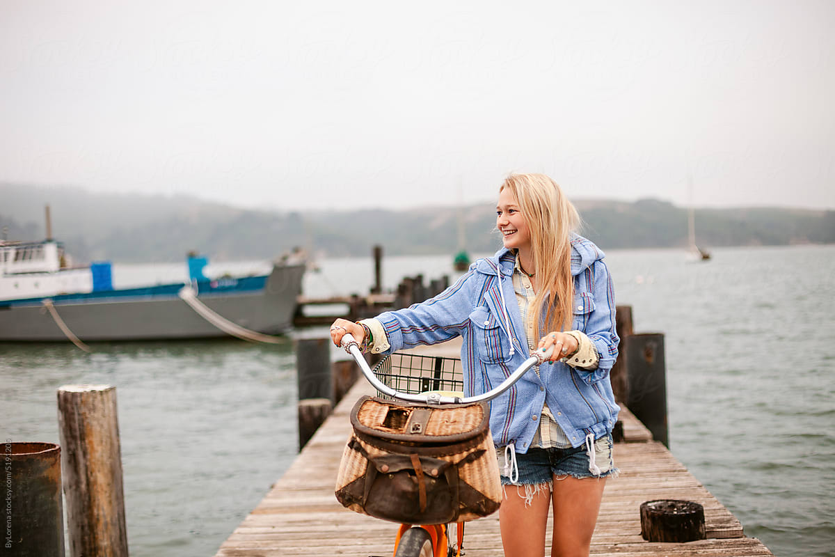Happy teenage girl with bike walking by the dock