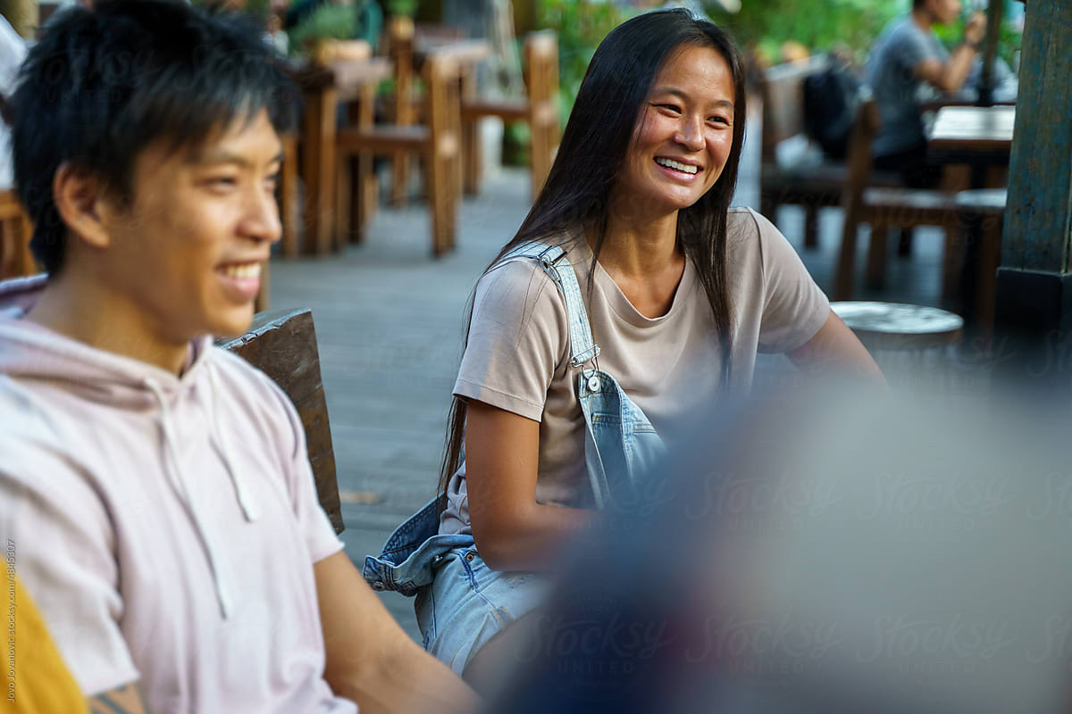 Two Asian friends smiling while listening to conversations