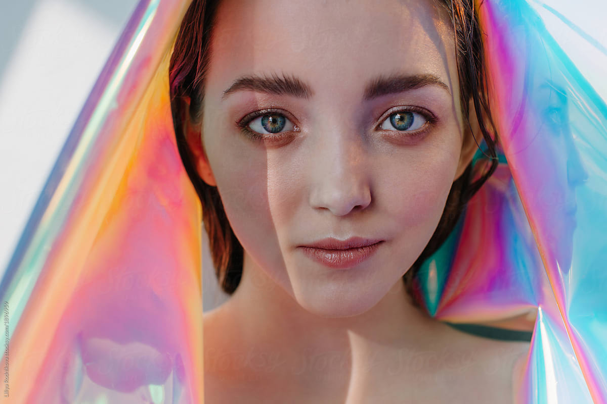 Surreal portrait of young pretty female with holographic foil and unusual lightning looking at camera
