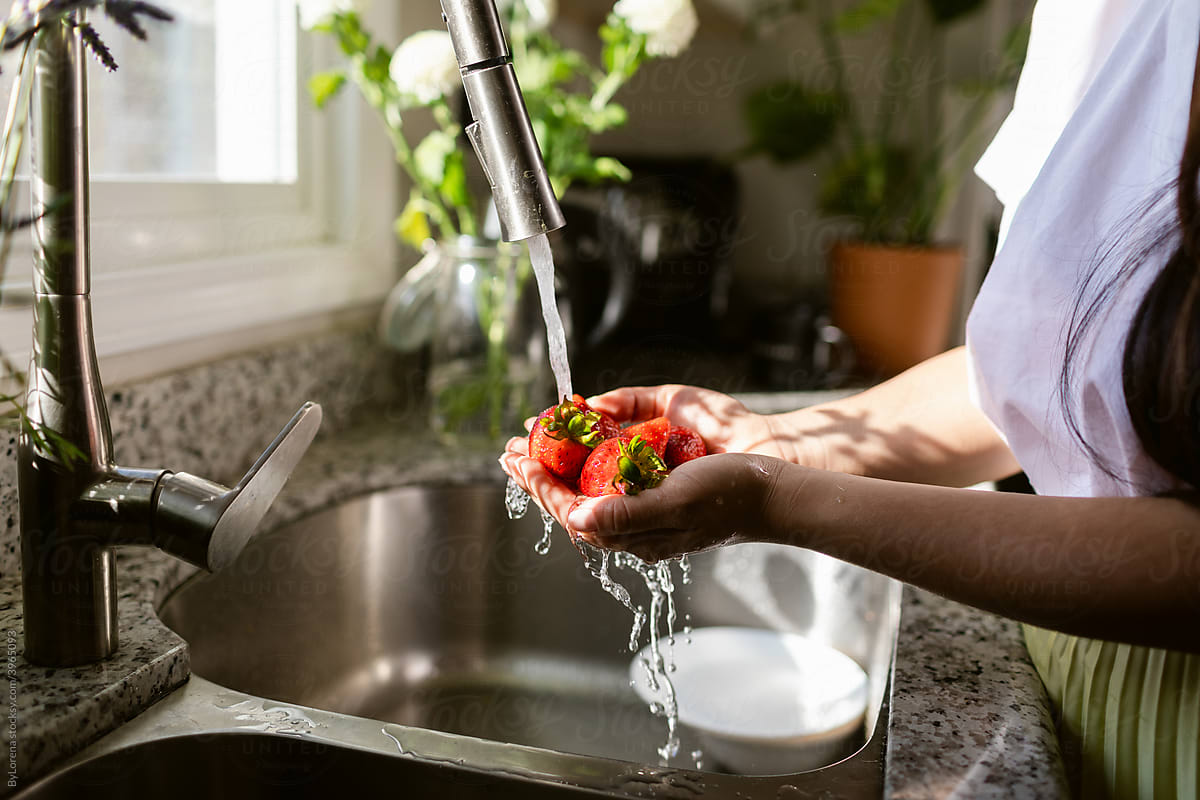 Woman washing fresh strawberry under tap in kitchen