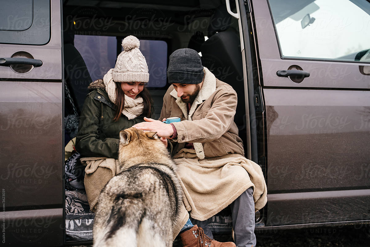 Young couple in a camper van in nature during winter petting wolf dog