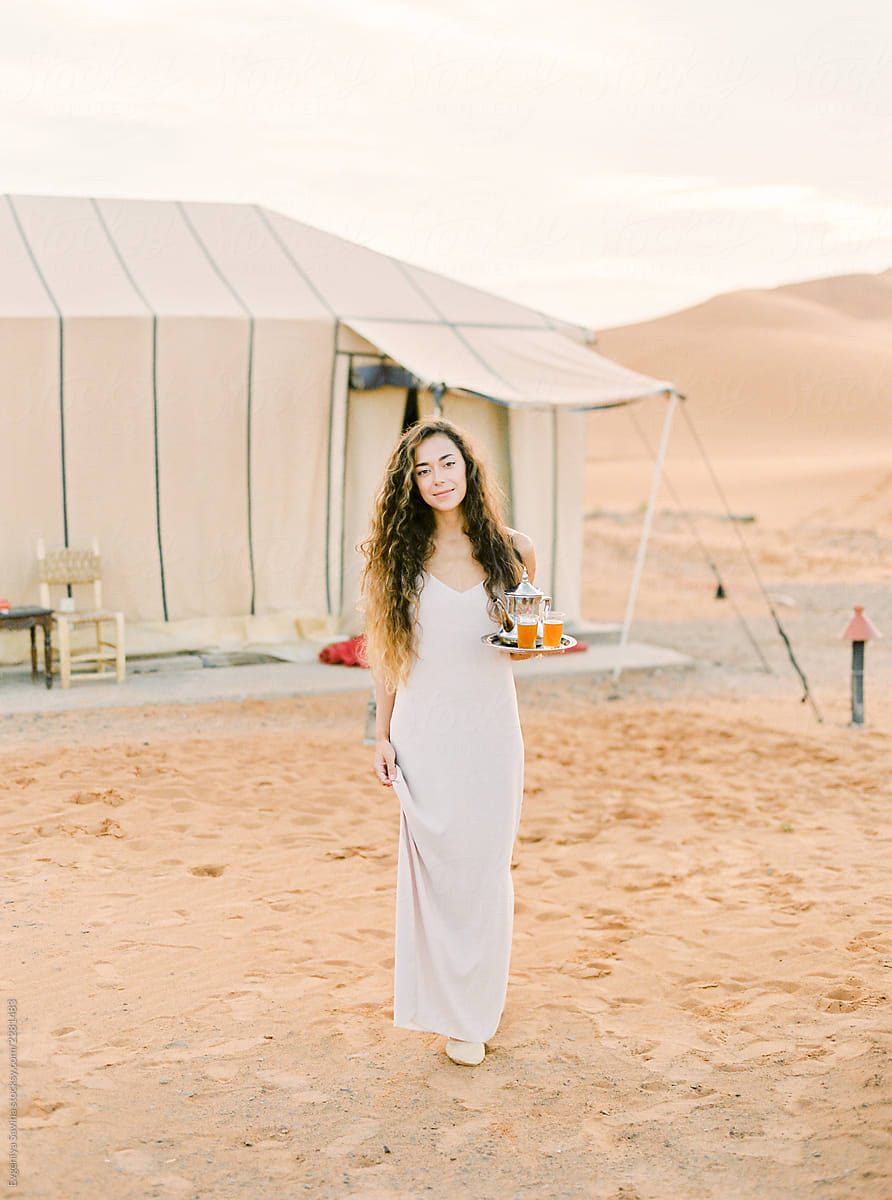 A portrait of a dark-haired woman serving moroccan mint tea in the desert camp