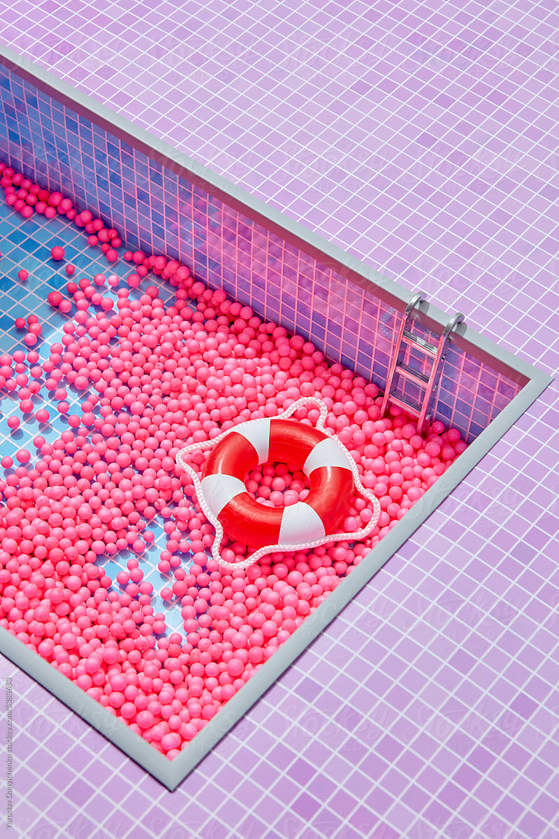 Red and white inflatable ring in blue pool with pink balls.