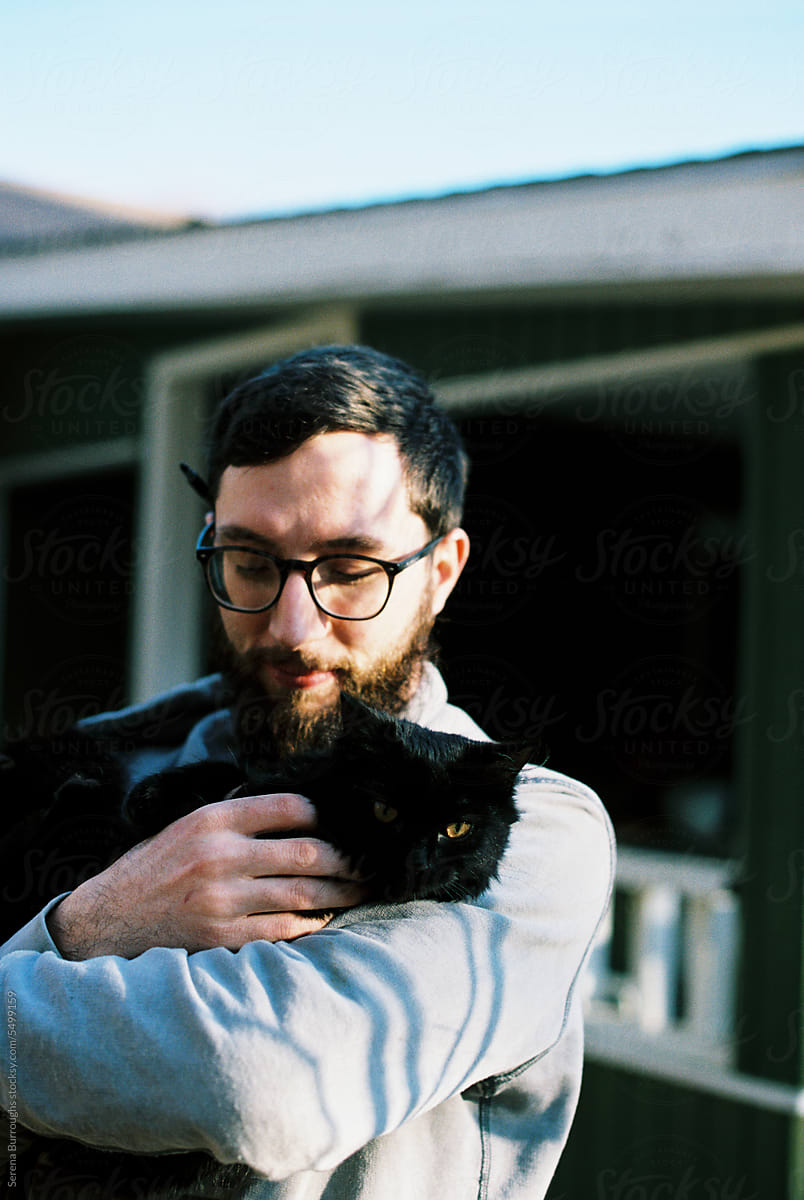 millennial man holding black cat in backyard outdoors in autumn