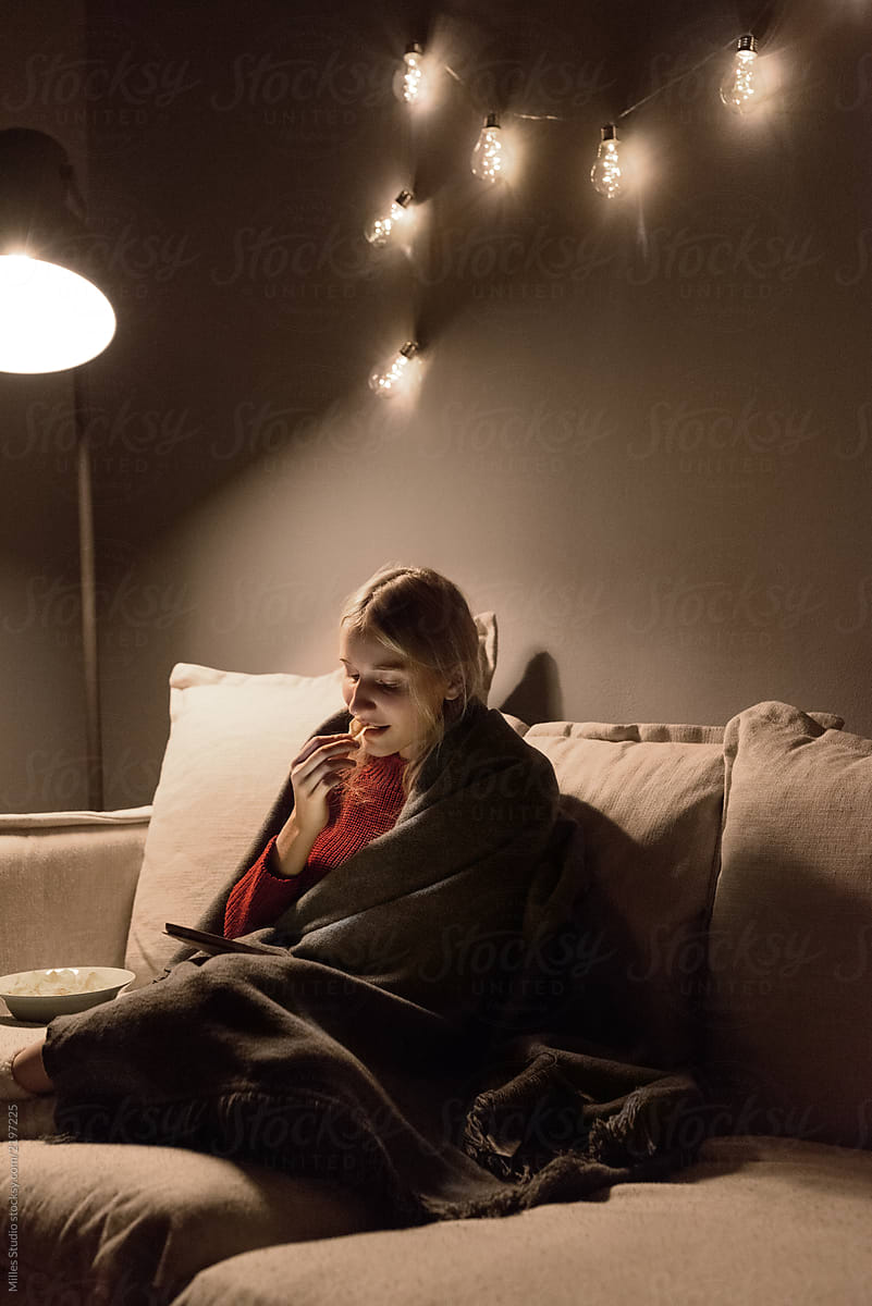 Woman with tablet eating chips on sofa