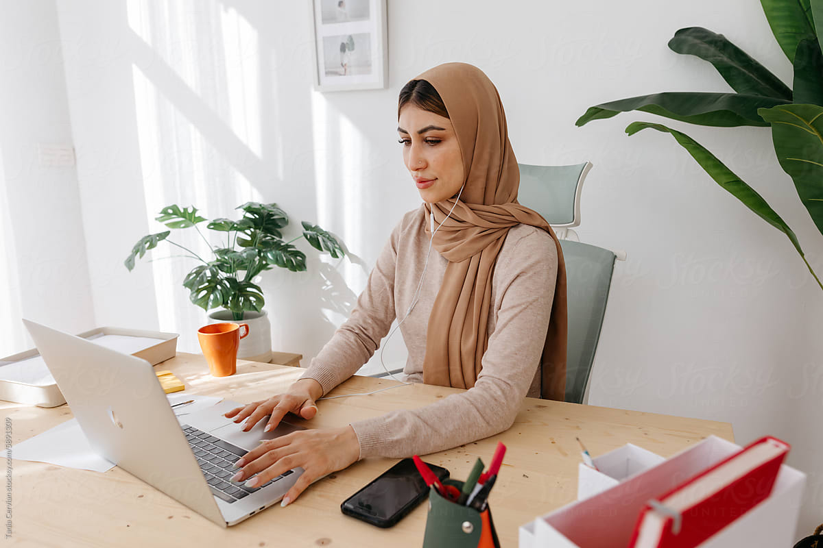 Focused woman in hijab working remotely on laptop