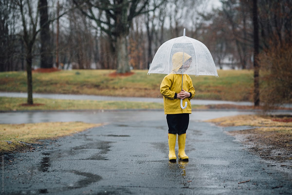 little boy in yellow raincoat and yellow boots stating under umbrella