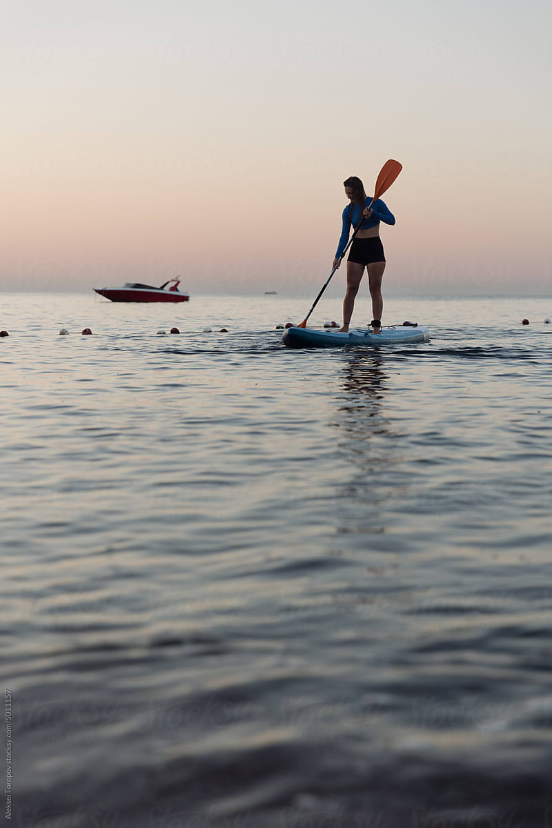 A young woman swims on a sup board.