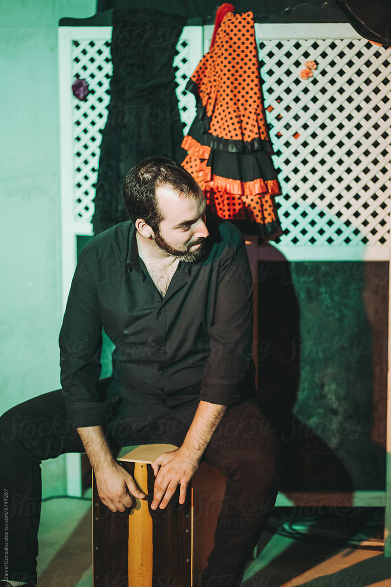 Young bearded man sitting on cajon drum while performing