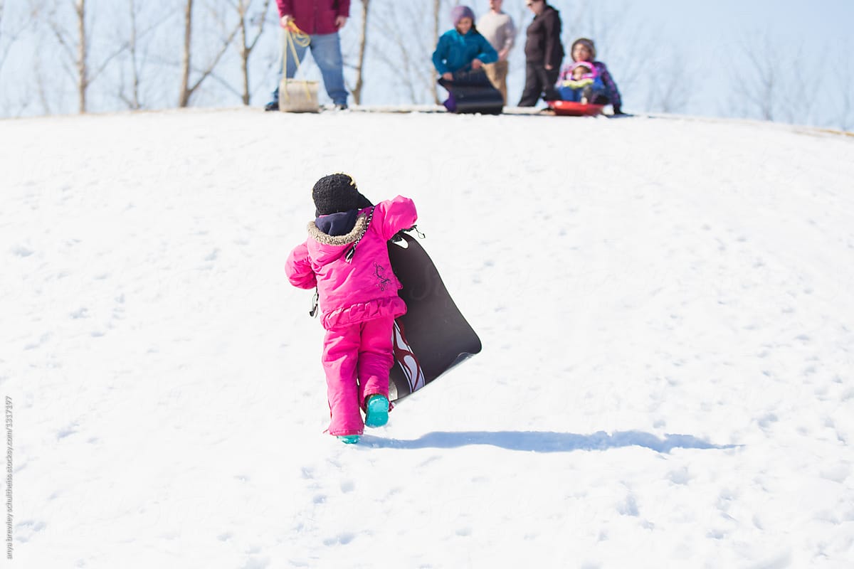 Young child carrying her sled back up a snowy hill