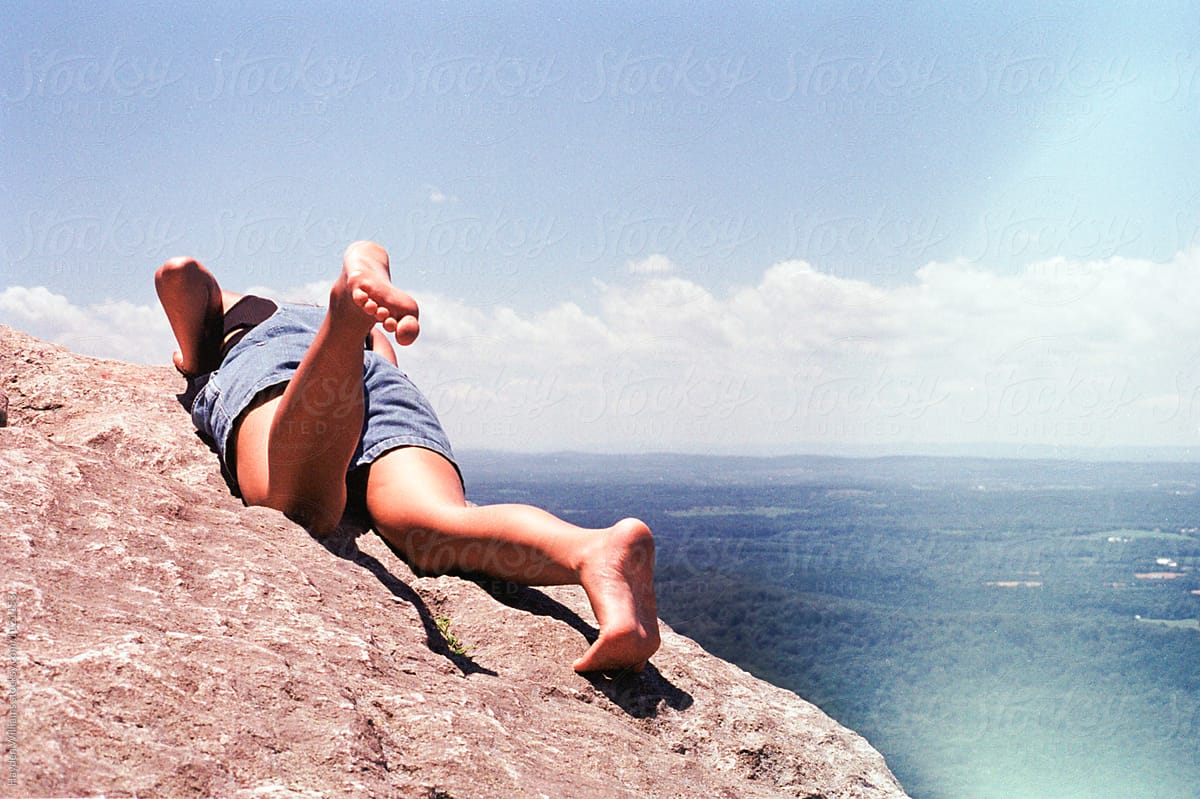 Girl laying down looking over the edge of a mountain view on a bright summer day
