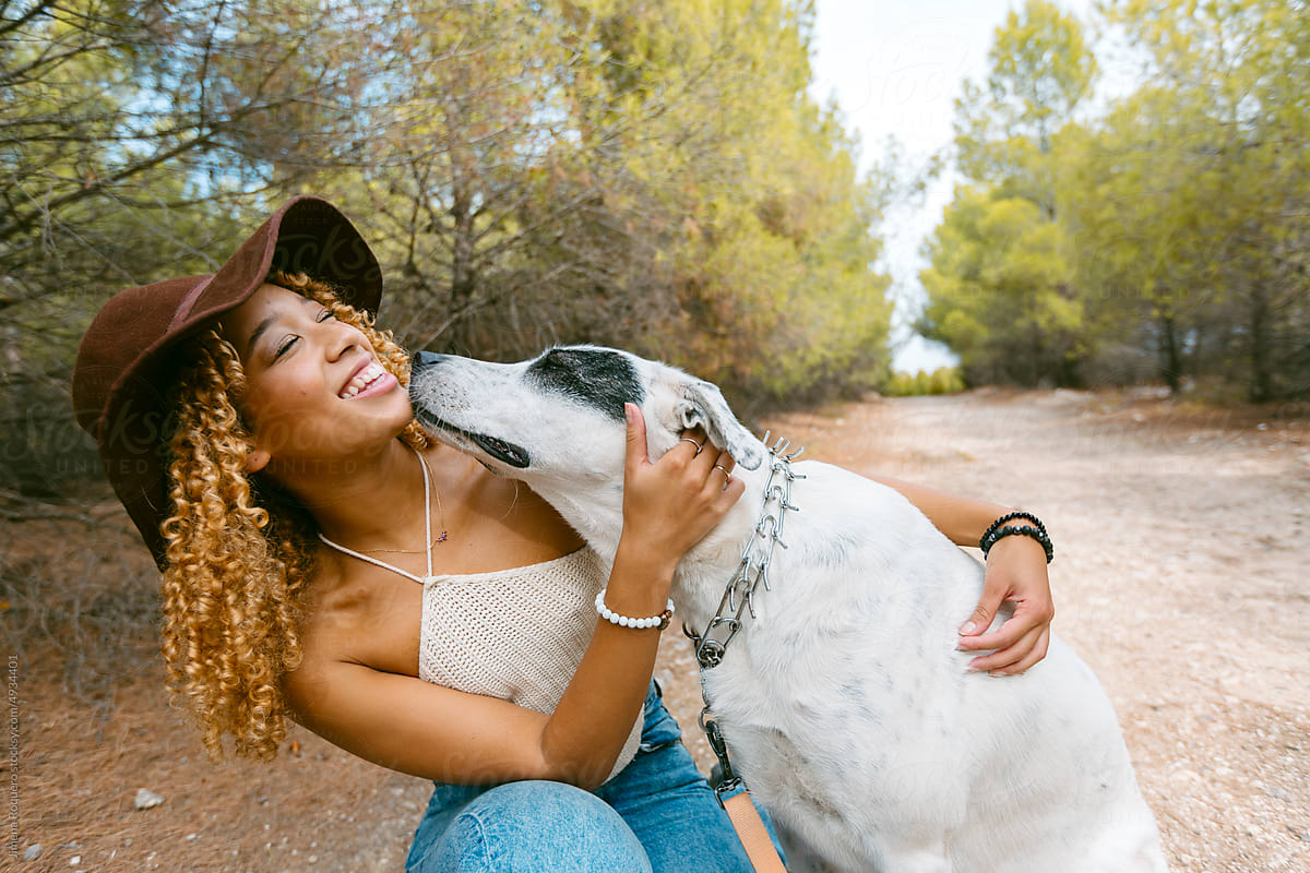Girl with hat petting her dog outdoor in sunlight laughing