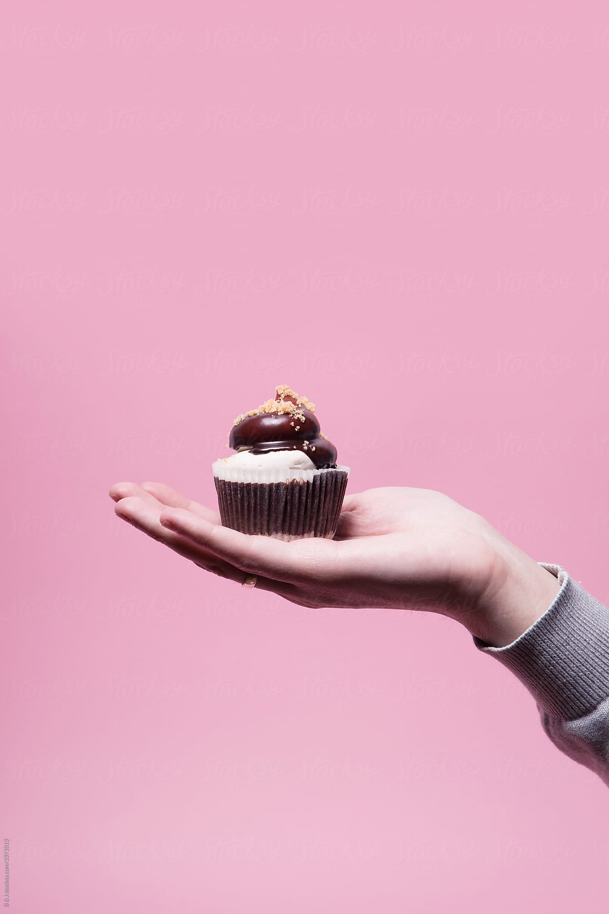 Male hand holding chocolate cupcake against bright pink background