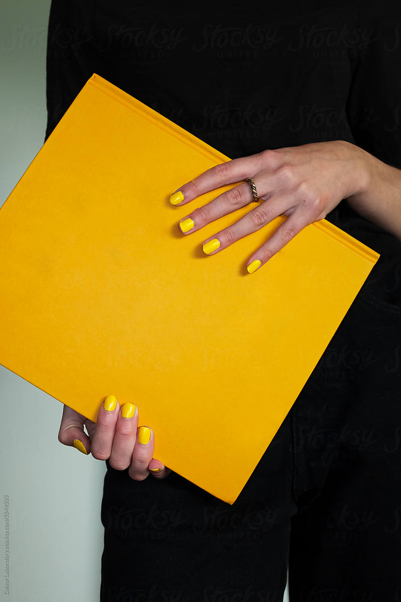 Person with yellow nails holding  yellow book with direct hard flash