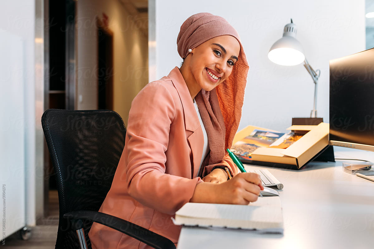 Muslim employee writing in diary at office desk