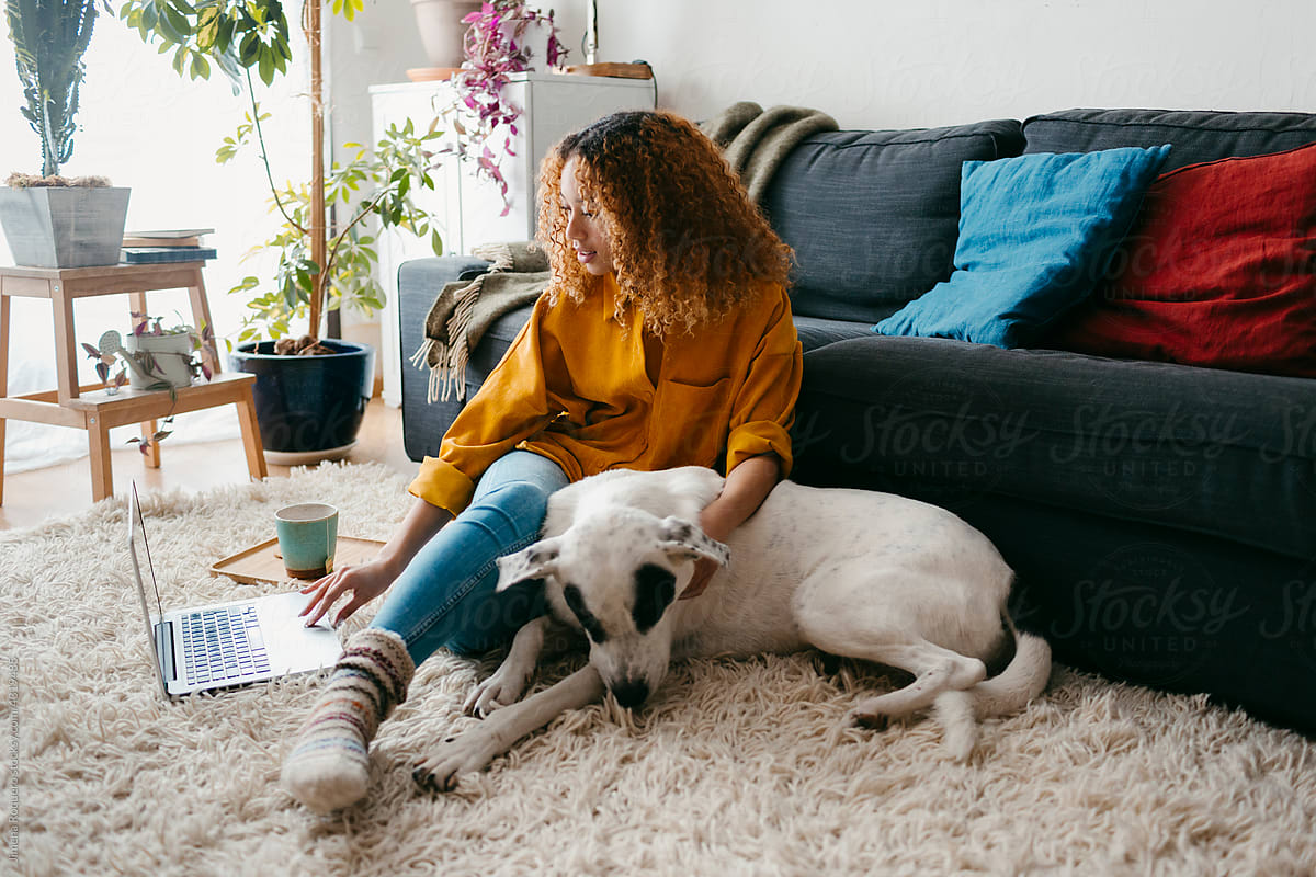 Young woman on home floor rug with dog using computer