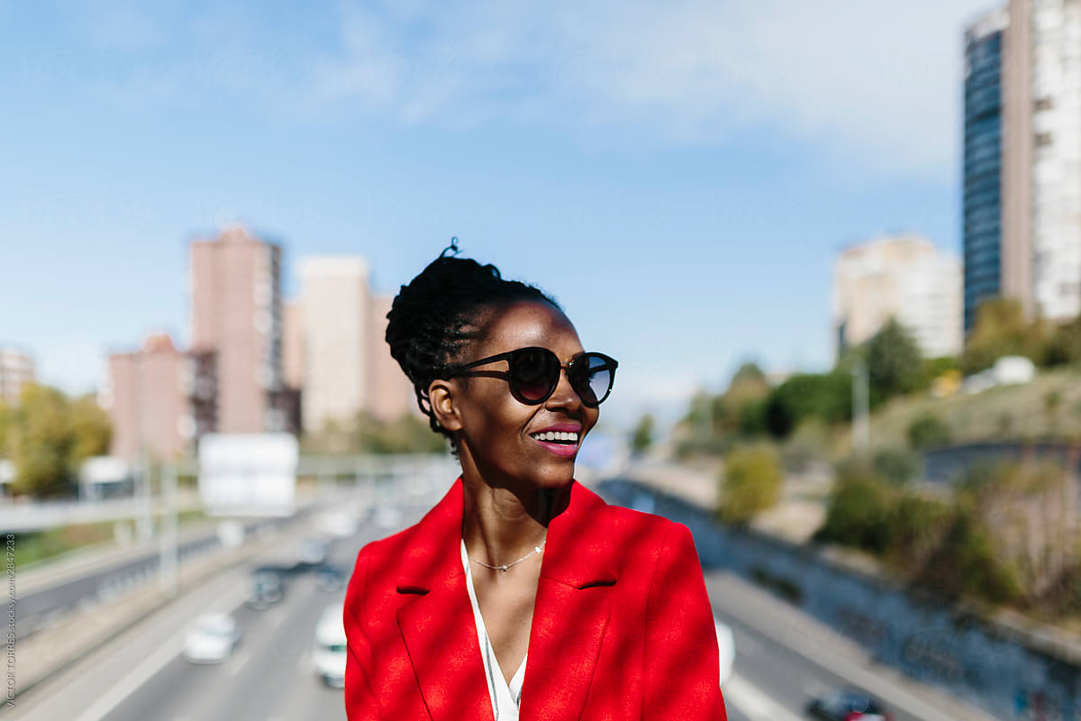 Stylish black woman in red jacket smiling in street