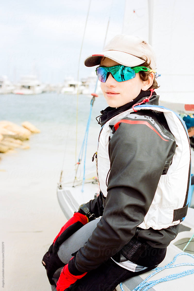 Teenage boy in sailing gear sitting on the side of a boat