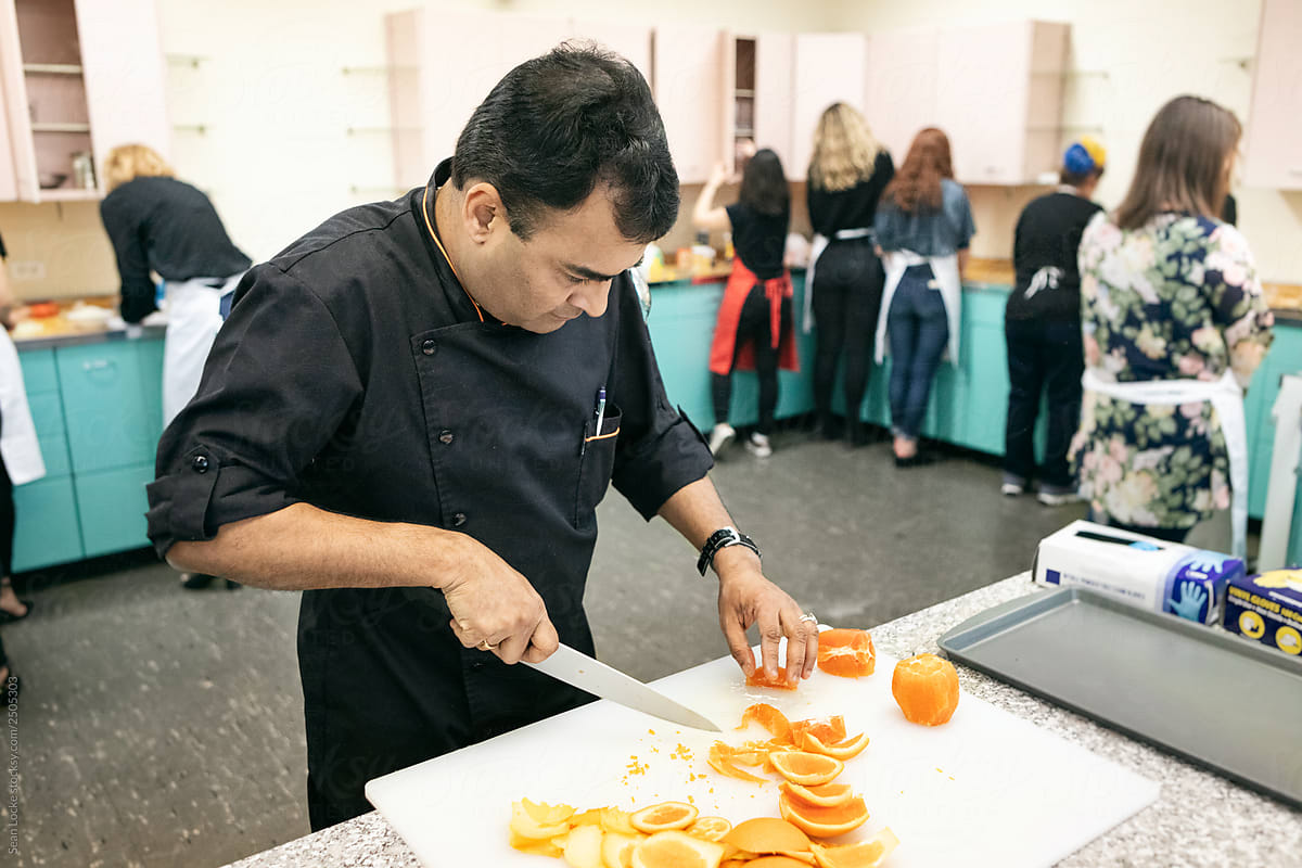Class: Chef Prepares Orange Slices While Group Cooks Behind